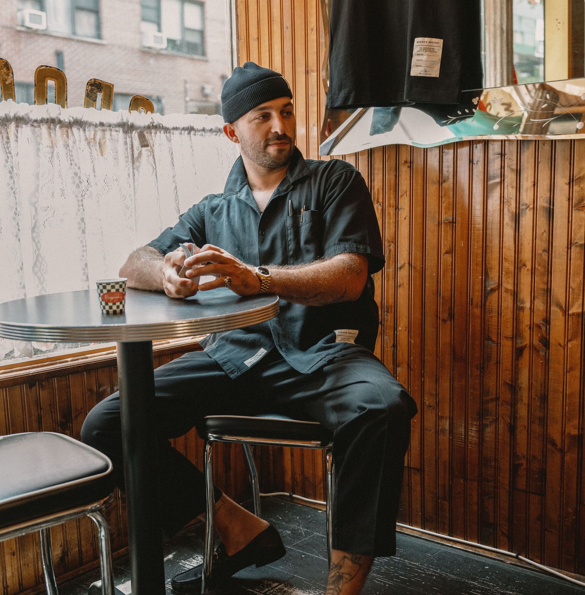 Man with playing cards wearing a black worker shirt, chino trousers and short beanie