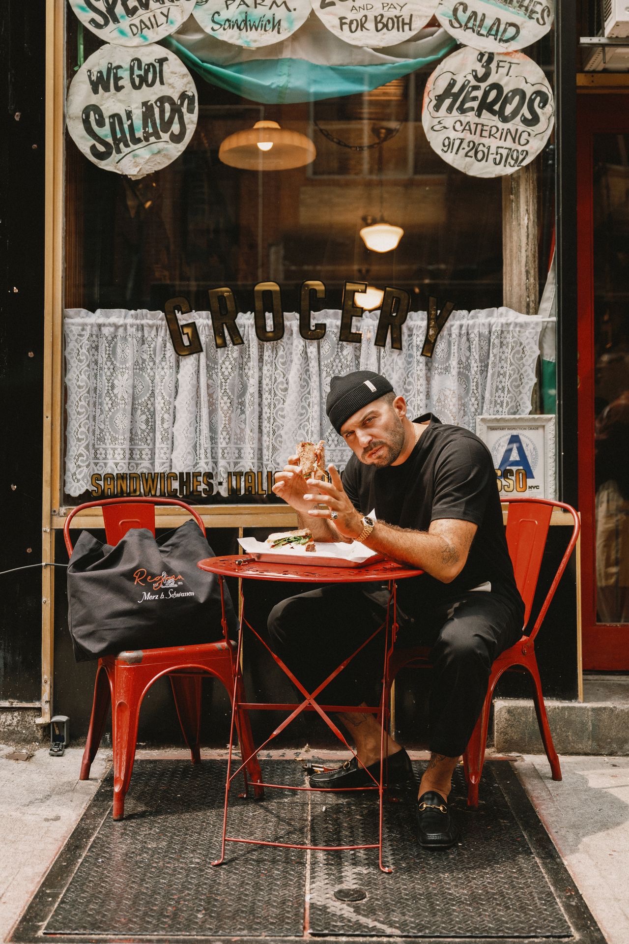 Man with black T-shirt and short beanie eating a sandwich 