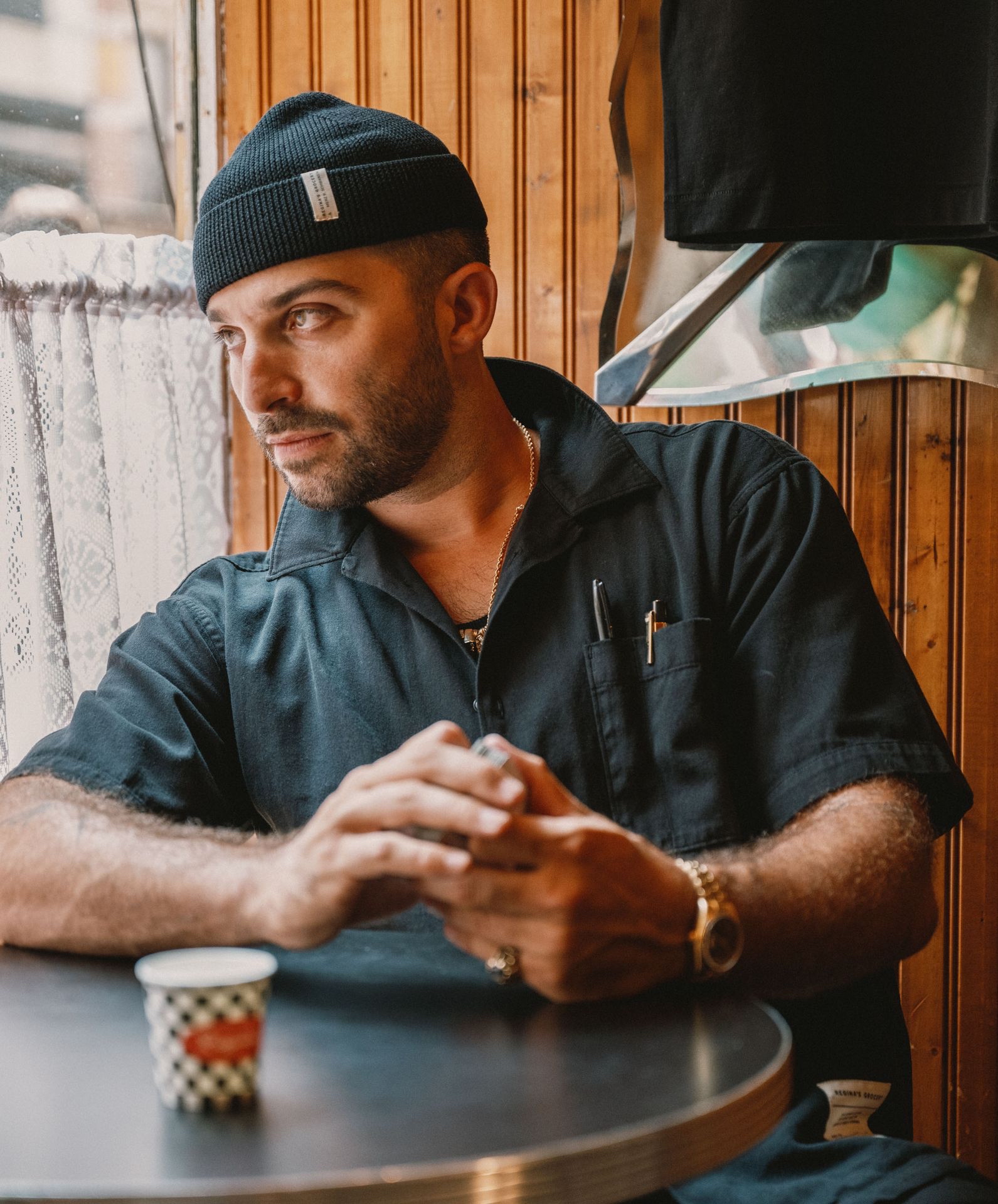 Man at table wearing black worker shirt and short beanie