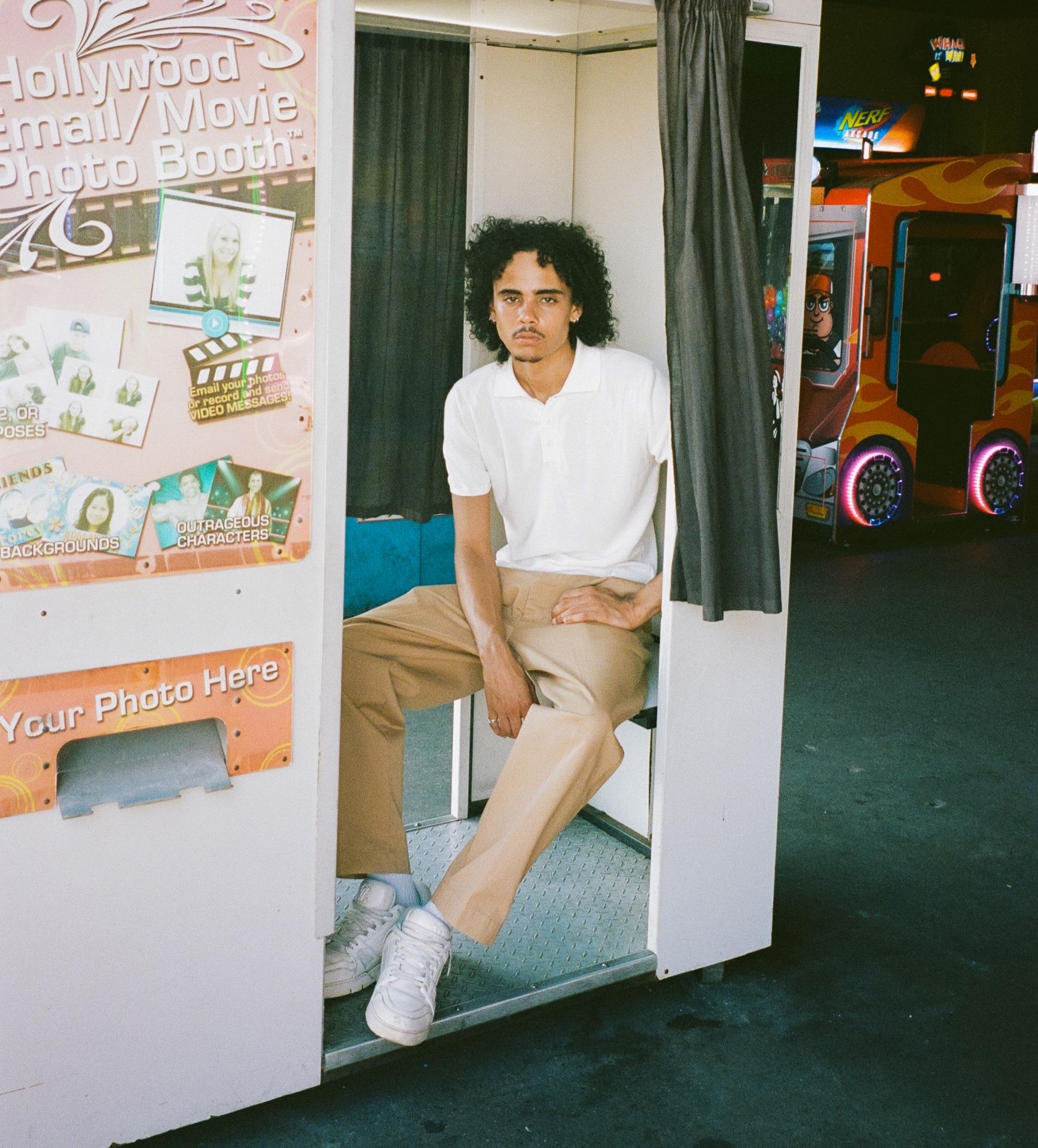 Man in white polo shirt and khaki chino trousers sitting in a photo booth