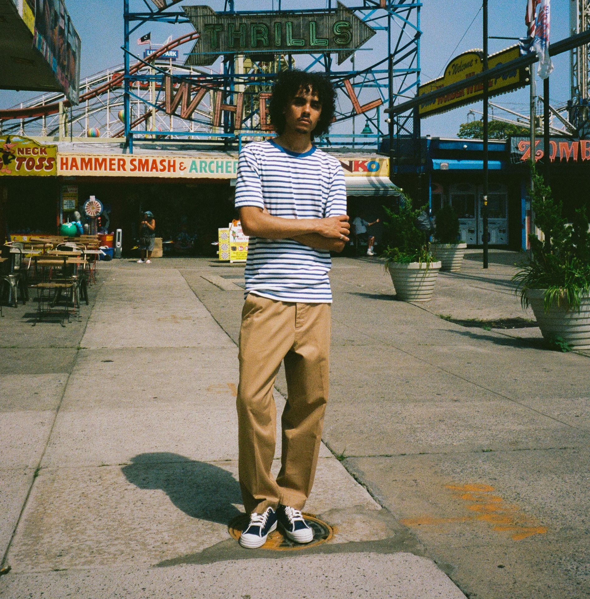 Man at funfair wearing khaki chino trousers, striped T-shirt and blue sneakers