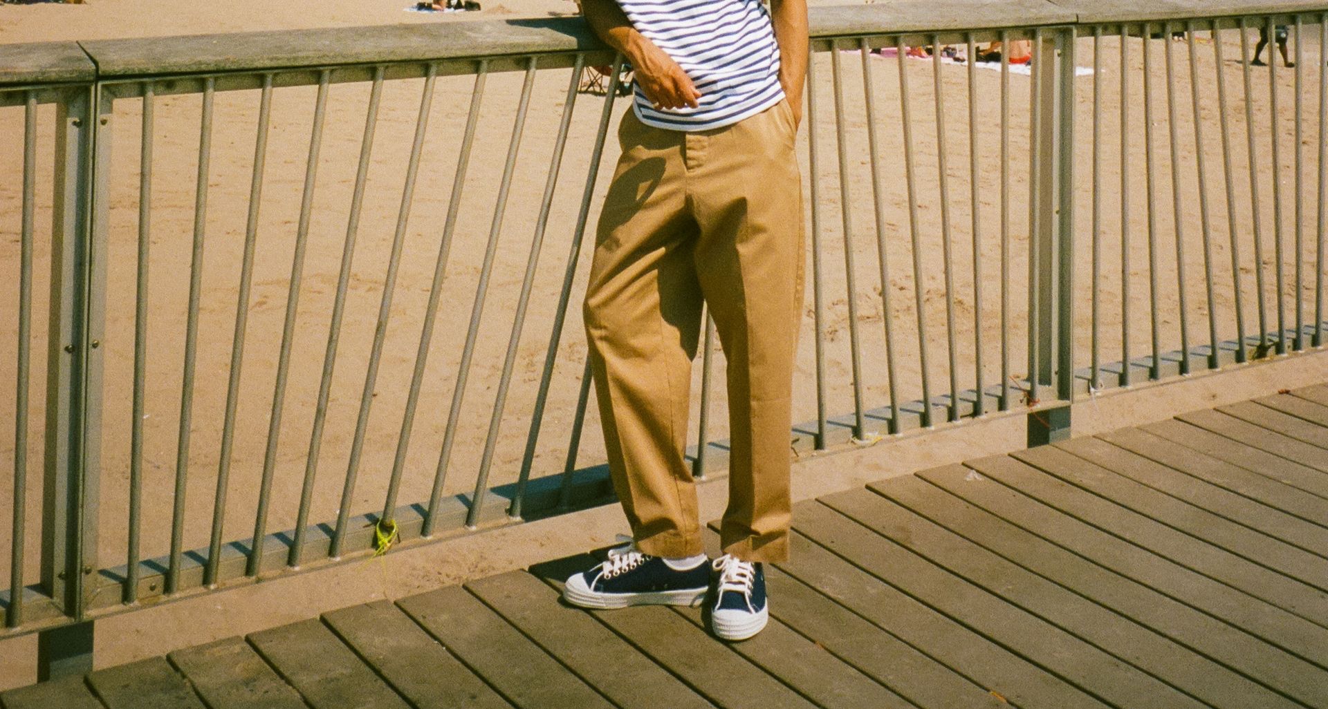 Man at the beach wearing khaki chino trousers, striped T-shirt and blue sneakers