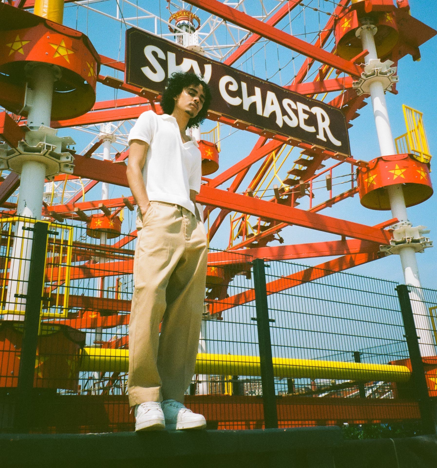 Man in front of high rope course wearing khaki chino trousers and white polo shirt