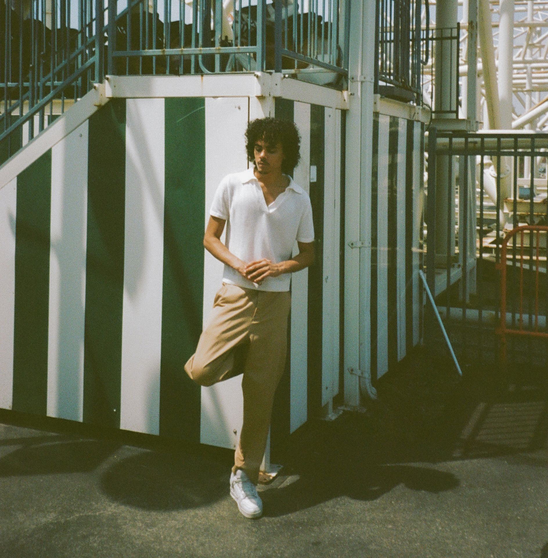 Man in front of rollercoaster wearing khaki chino trousers and white polo shirt