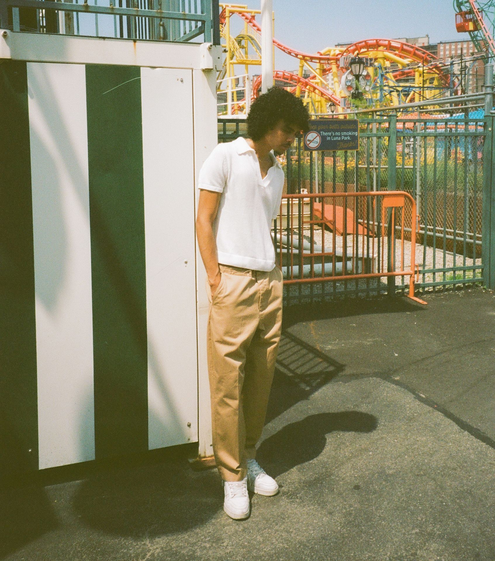Man in front of rollercoaster wearing khaki chino trousers and white polo shirt