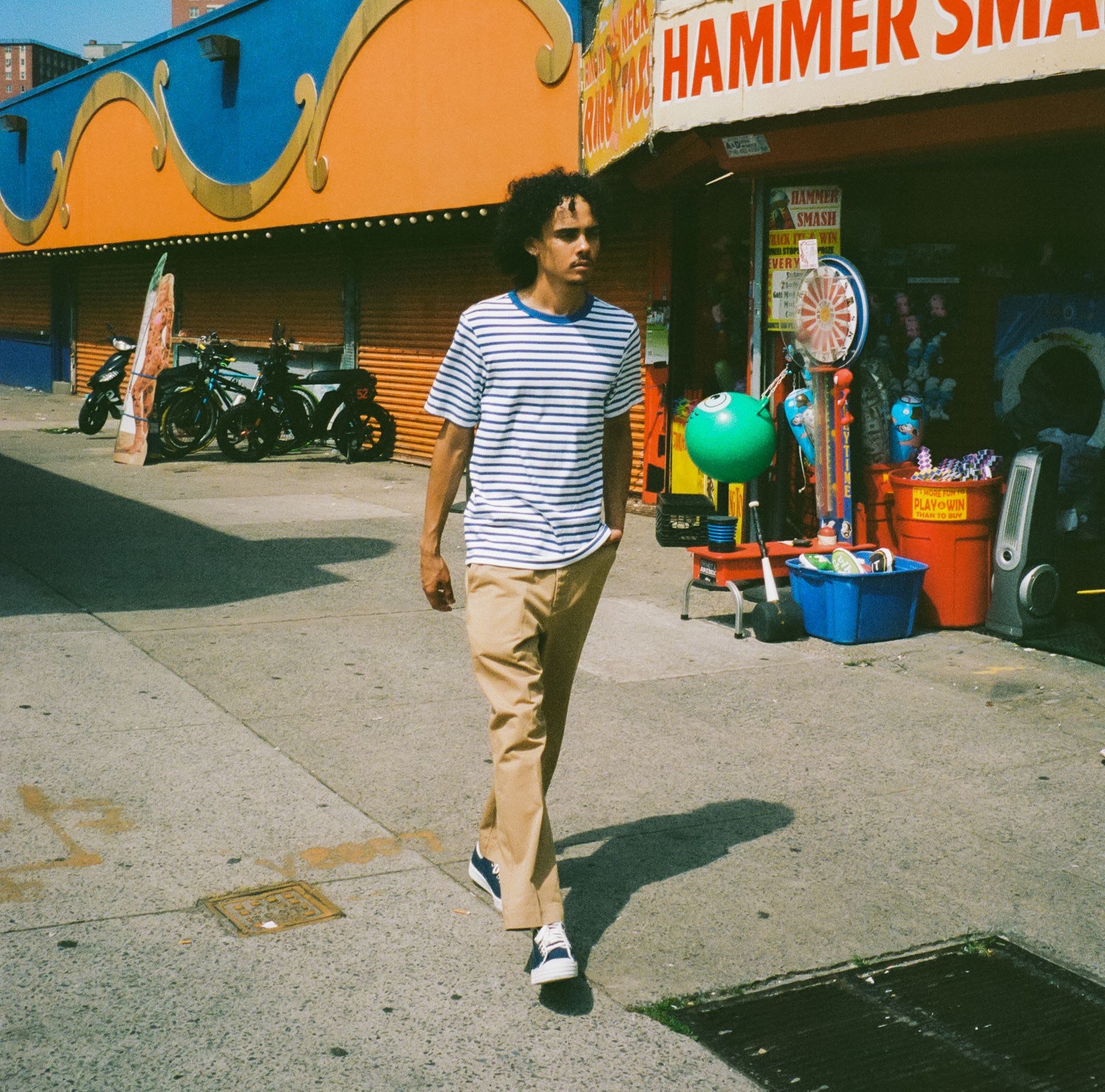 Man at funfair wearing khaki chino trousers, striped T-shirt and blue sneakers